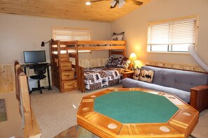 A room with a bunk bed, a desk with a computer, a couch, and a green octagonal table.