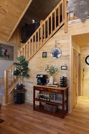 A wooden staircase leading to a loft area with a coffee machine, a vase with flowers, and a framed picture on the wall.