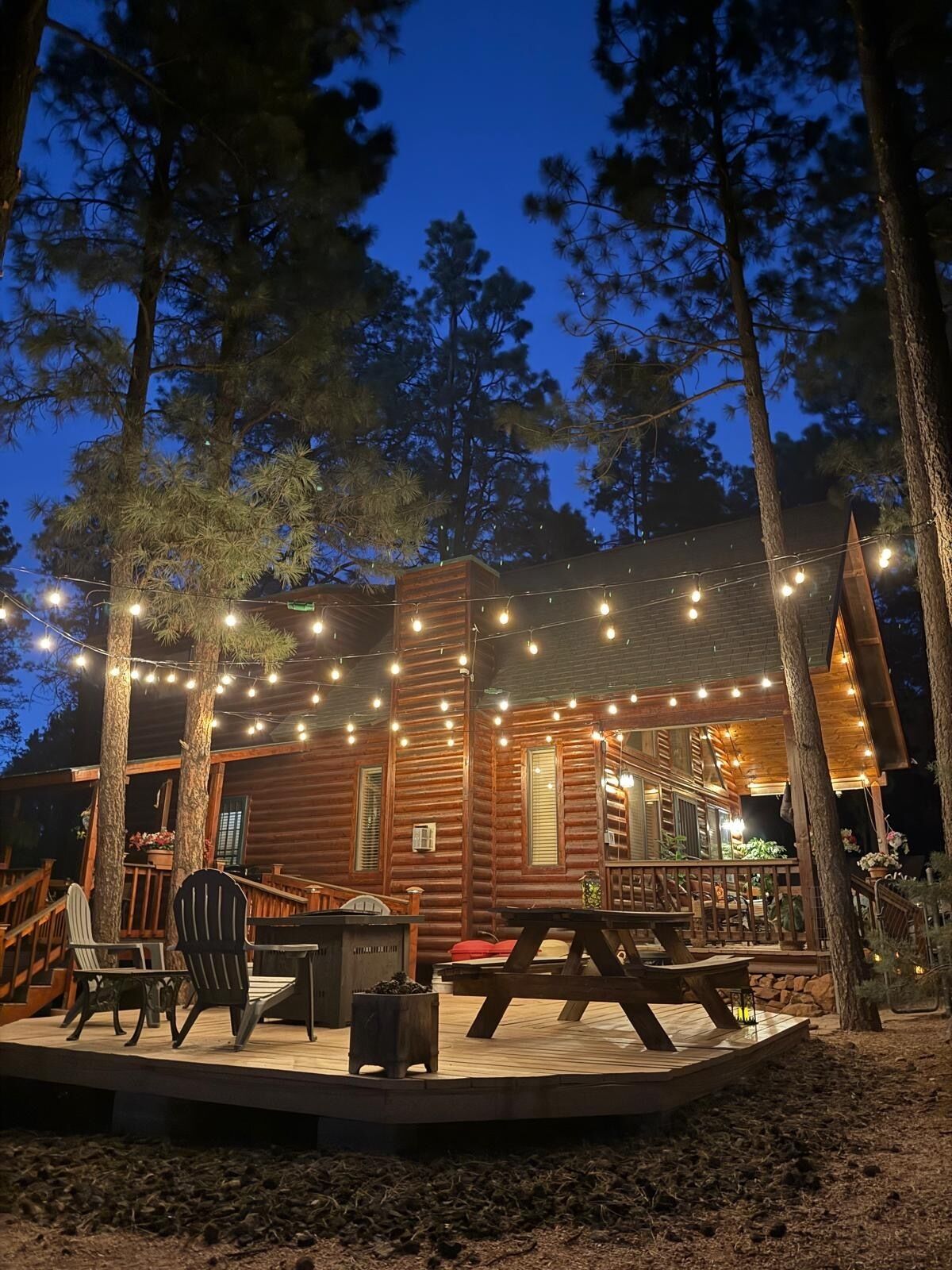 Une cabane en rondins avec une terrasse, des sièges d’extérieur et des guirlandes lumineuses.
