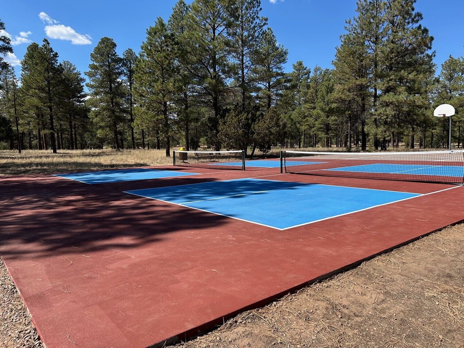 An outdoor tennis court with red and blue surfaces, surrounded by trees.