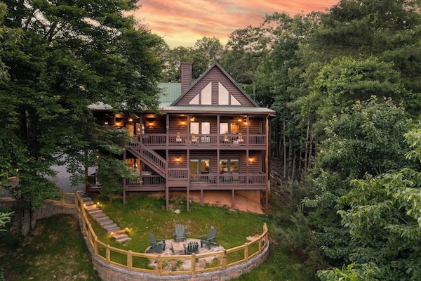 Wooded multi-story cabin with large windows, wooden siding, and wraparound deck.