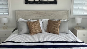 Un lit avec une couette à rayures blanches et bleu marine, deux coussins bruns à texture, et une tête de lit en bois.