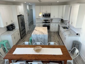 A modern kitchen with white cabinets, stainless steel appliances, and a wooden dining table with chairs.