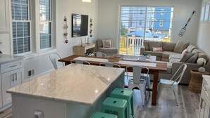Une cuisine moderne dotée d’un grand îlot central, de tabourets de bar verts et d’un coin repas avec un canapé et des chaises.