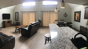 Een ruime woonkamer met een leren bank, een eettafel en een keuken met een marmeren aanrecht.