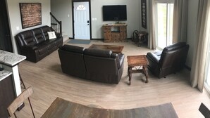 Een woonkamer met een donker leren bank, een houten salontafel en een tv op een houten dressoir.