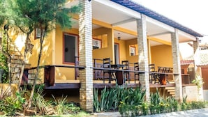A yellow building with a covered patio area, outdoor seating, and a stone staircase. - Pousada Saruê Natal (Natal)