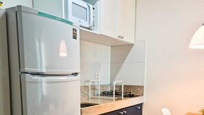 Una cocina compacta con refrigerador integrado, microondas, estufa a gas y horno pequeño. Hay una mesa de comedor con sillas y una lámpara colgante.