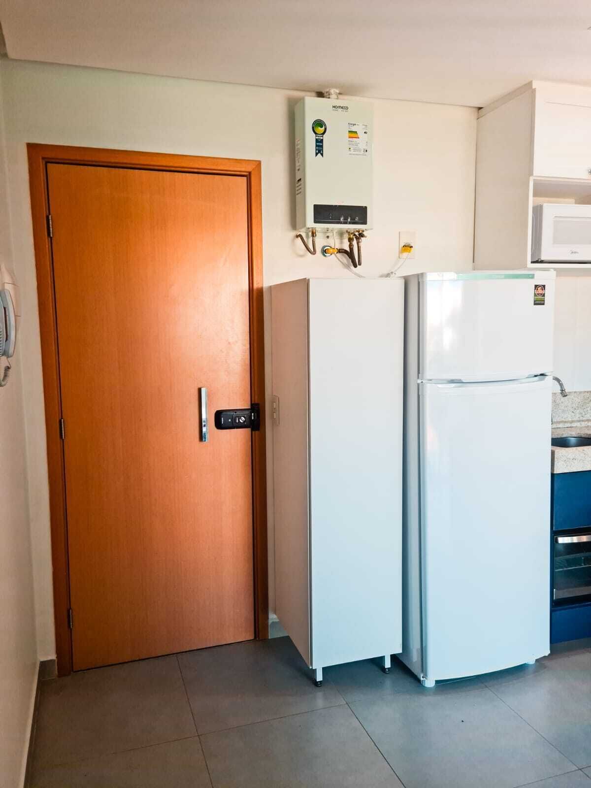 A compact kitchen with a wooden door, a white refrigerator, and a wall-mounted water heater.
