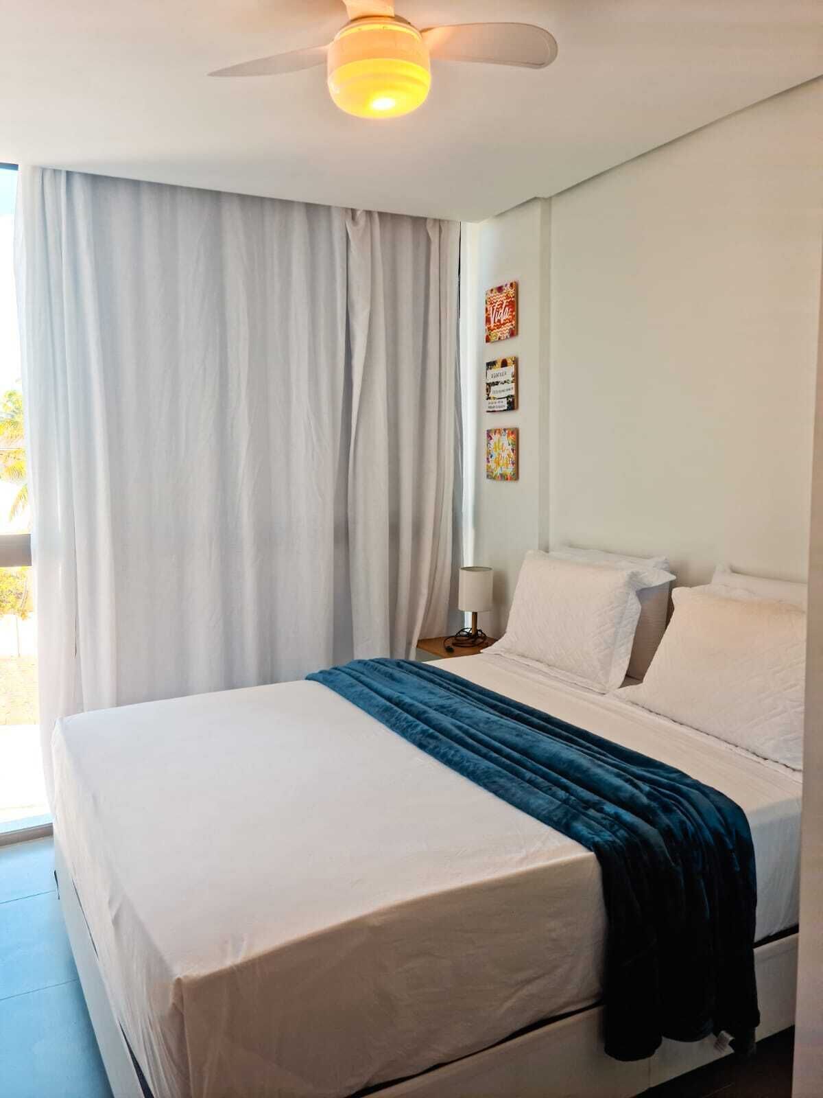 Une chambre d’hôtel avec un lit, un ventilateur de plafond, une fenêtre avec des rideaux et des œuvres d’art murales.