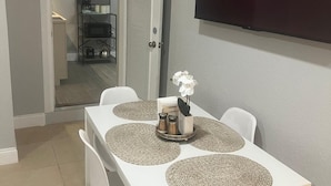 En matplats med ett vitt bord, fyra stolar och en tv på väggen som visar "TCL Roku TV".