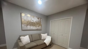 Ett vardagsrum med en neutral färgskala, en beige soffa, en vit pläd och en stor, abstrakt tavla på väggen.