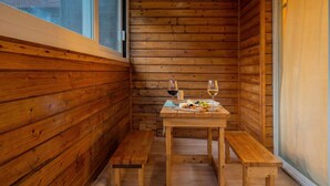 Interior de una cabaña de madera con una mesa de madera preparada para dos personas, dos copas de vino y una tabla de quesos.