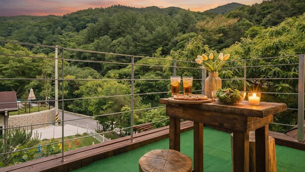Una terraza con una mesa lista para comer, rodeada por una barandilla de metal, con vistas a un área boscosa exuberante.