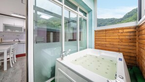 Un baño moderno con ducha de vidrio, una bañera independiente y vistas a una ladera boscosa.
