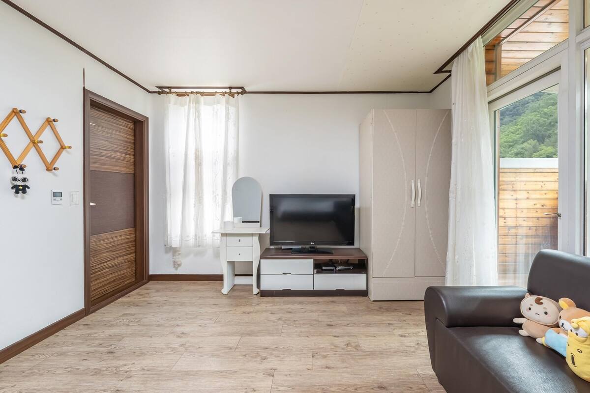 A modern living room with a flat-screen TV, a sofa, and a wooden floor.