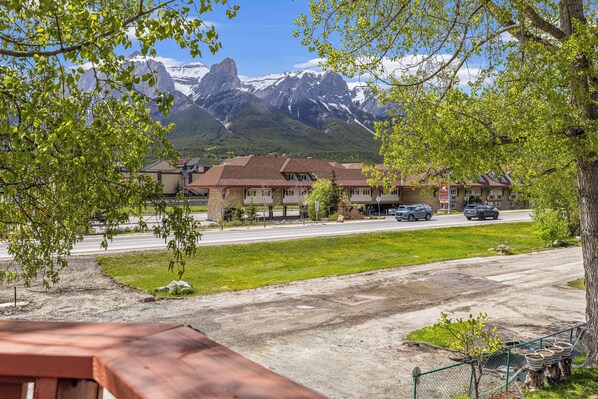 A view of a building with multiple roofs, a road in the foreground, and a mountain range in the background.
