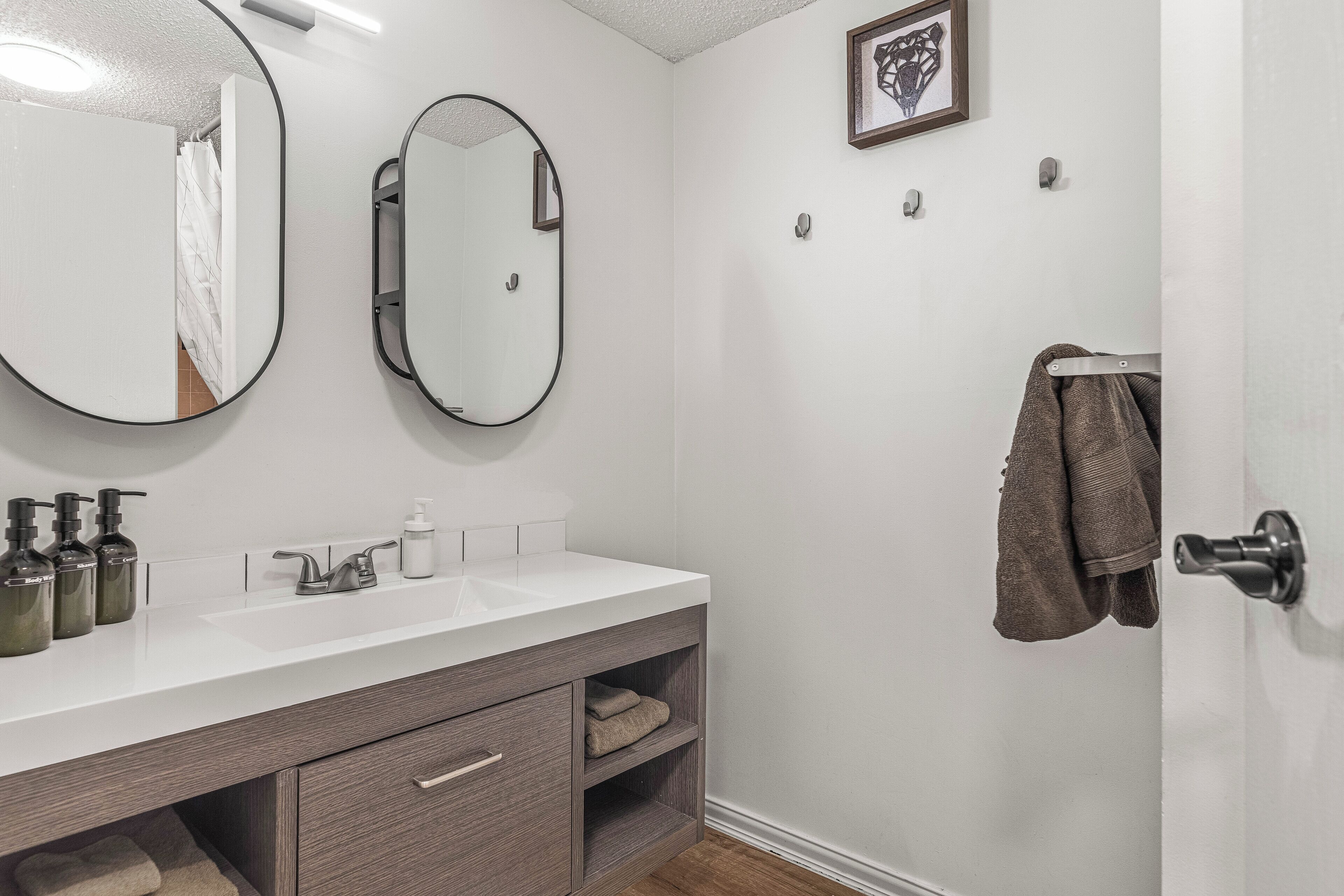A bathroom with a white sink, two mirrors, a towel rack, and a framed picture on the wall.