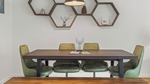 Zona pranzo con tavolo in legno scuro, quattro sedie imbottite verdi e un pannello esagonale decorativo con lampada a sospensione.