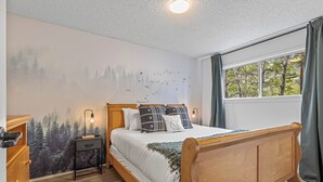 Una camera da letto con un letto in legno, un comodino con una lampada, una cassettiera e un affresco raffigurante una foresta.