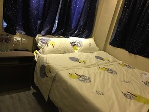 A hotel room with a bed featuring a leaf pattern, a bedside table with a lamp, and a window with star-patterned curtains. - Zixin Hotel (Kowloon)