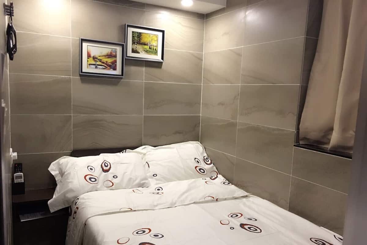 A small, private bathroom with a bed, two framed pictures on the wall, and a towel hanging on the door.