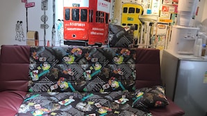 A room with a sofa featuring cartoon character prints, a red double-decker bus artwork, and a yellow bus artwork on the wall. - Zixin Hotel (Kowloon)