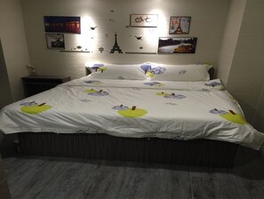A neatly made bed with a white bedspread featuring yellow and purple designs, a dark wooden headboard, and a wall decorated with framed pictures including the Eiffel Tower. - Zixin Hotel (Kowloon)