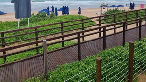 A wooden boardwalk leading to a beach with blue umbrellas and a signboard. - Cupe Beach Living by La Playa (Ipojuca)