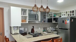 A modern kitchen with a central island, wooden chairs, a stainless steel refrigerator, and pendant lighting. - Cupe Beach Living by La Playa (Ipojuca)