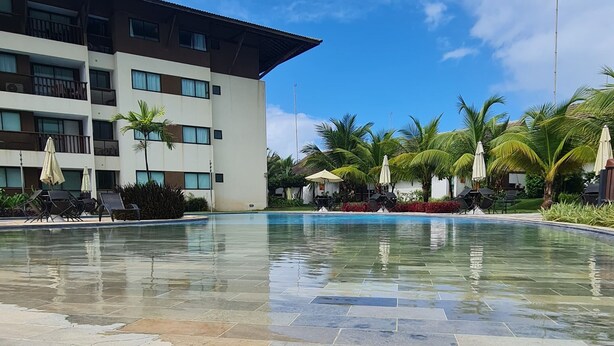 A swimming pool area with a building in the background, surrounded by palm trees and lounge chairs. - Cupe Beach Living by La Playa (Ipojuca)
