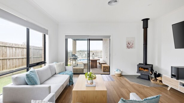 A modern living room with a sofa, coffee table, and a fireplace. There is a sliding glass door leading to an outdoor patio with a pool and furniture. - Thyme Out with pool in Cowes (Cowes)