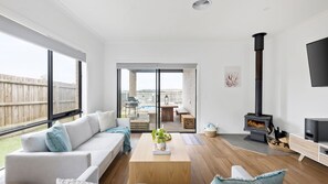 A modern living room with a sofa, coffee table, and a fireplace. There is a sliding glass door leading to an outdoor patio with a pool and furniture. - Thyme Out with pool in Cowes (Cowes)