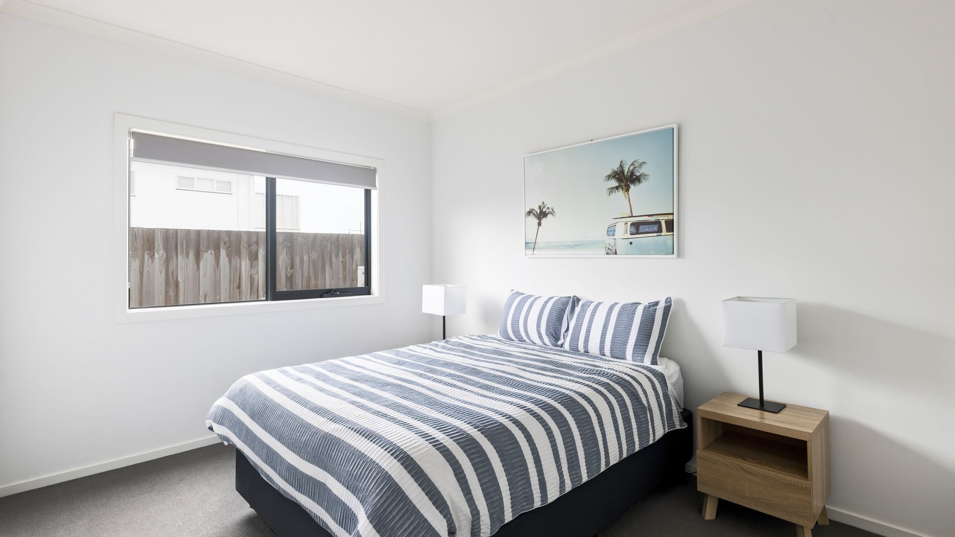 A bedroom with a bed, a nightstand, a window, and a wall-mounted picture.