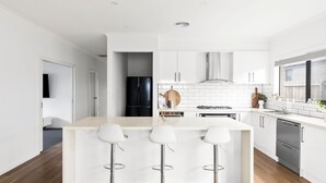 A modern kitchen with white cabinets, a black refrigerator, a gas stove, and a bar area with three stools. - Thyme Out with pool in Cowes (Cowes)