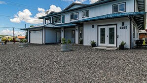A two-story house with a garage, a covered porch, and a number '1018' on the side. - Experience Tropical Tranquility: Luxury Studio Home in Hilo!  (Hilo)
