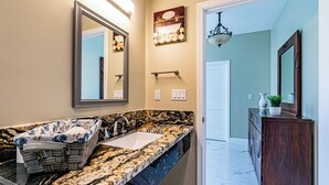 A bathroom with a marble countertop, a sink, a mirror, and a vanity with a plant. - Experience Tropical Tranquility: Luxury Studio Home in Hilo!  (Hilo)