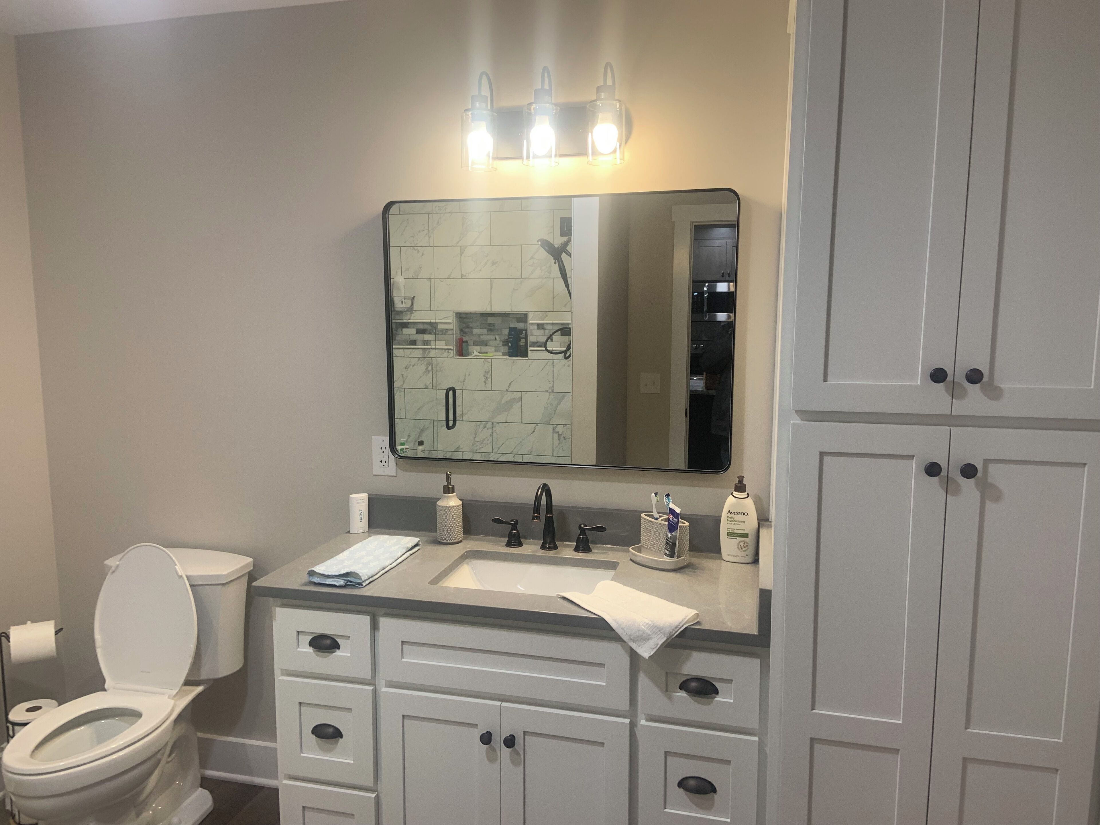 A bathroom with a toilet, sink, mirror, and cabinets.