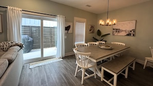 A dining area with a wooden table, white chairs, and a chandelier. - New Condo, Sleeps 6, 3 Bedroom, Beach Access, Community Pool & Private Cabanas. (Corolla)