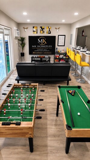 Un espace de détente moderne avec une table de baby-foot, une table de billard et un bar avec des sièges.