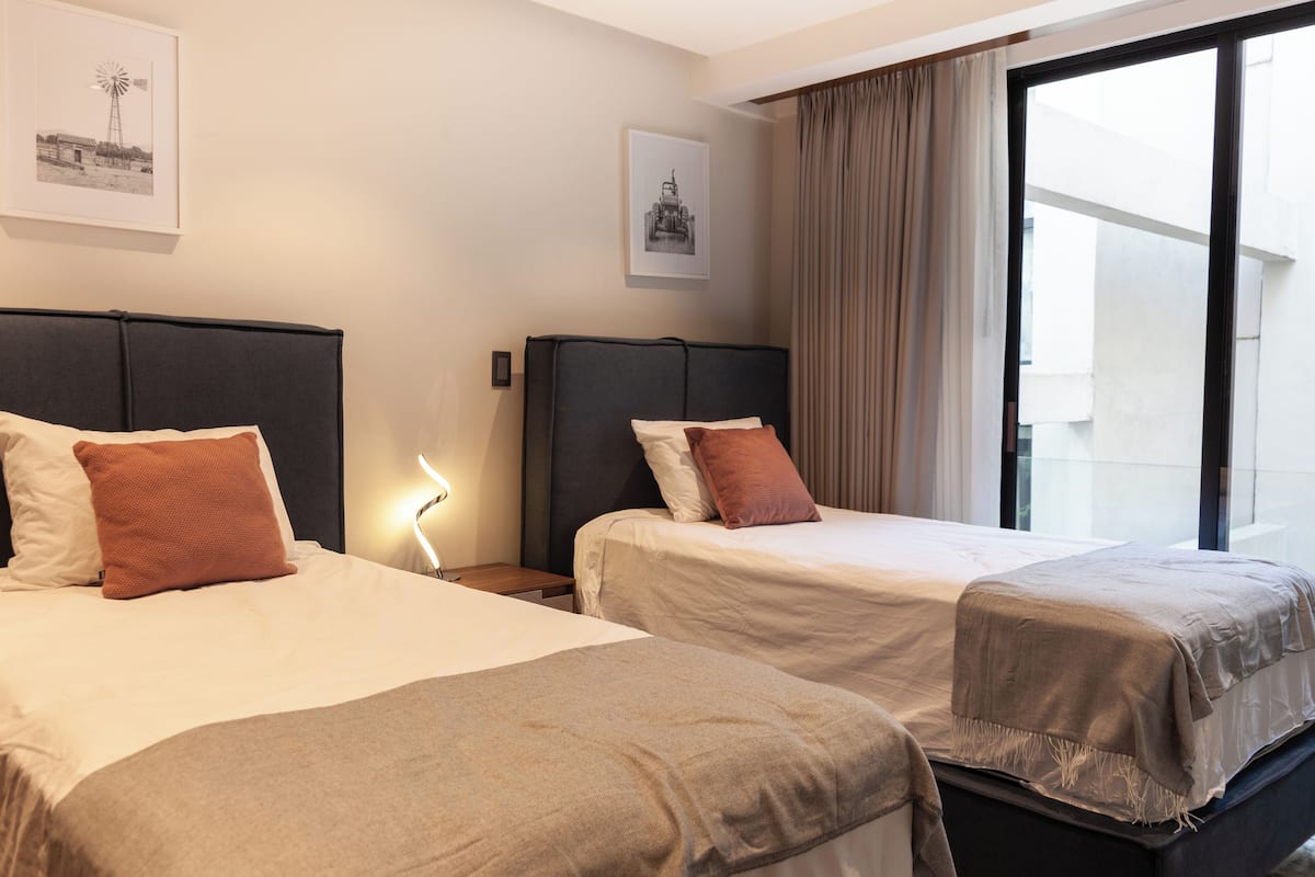 Una habitación de hotel con dos camas, una mesita de noche, una lámpara y una ventana con cortinas.