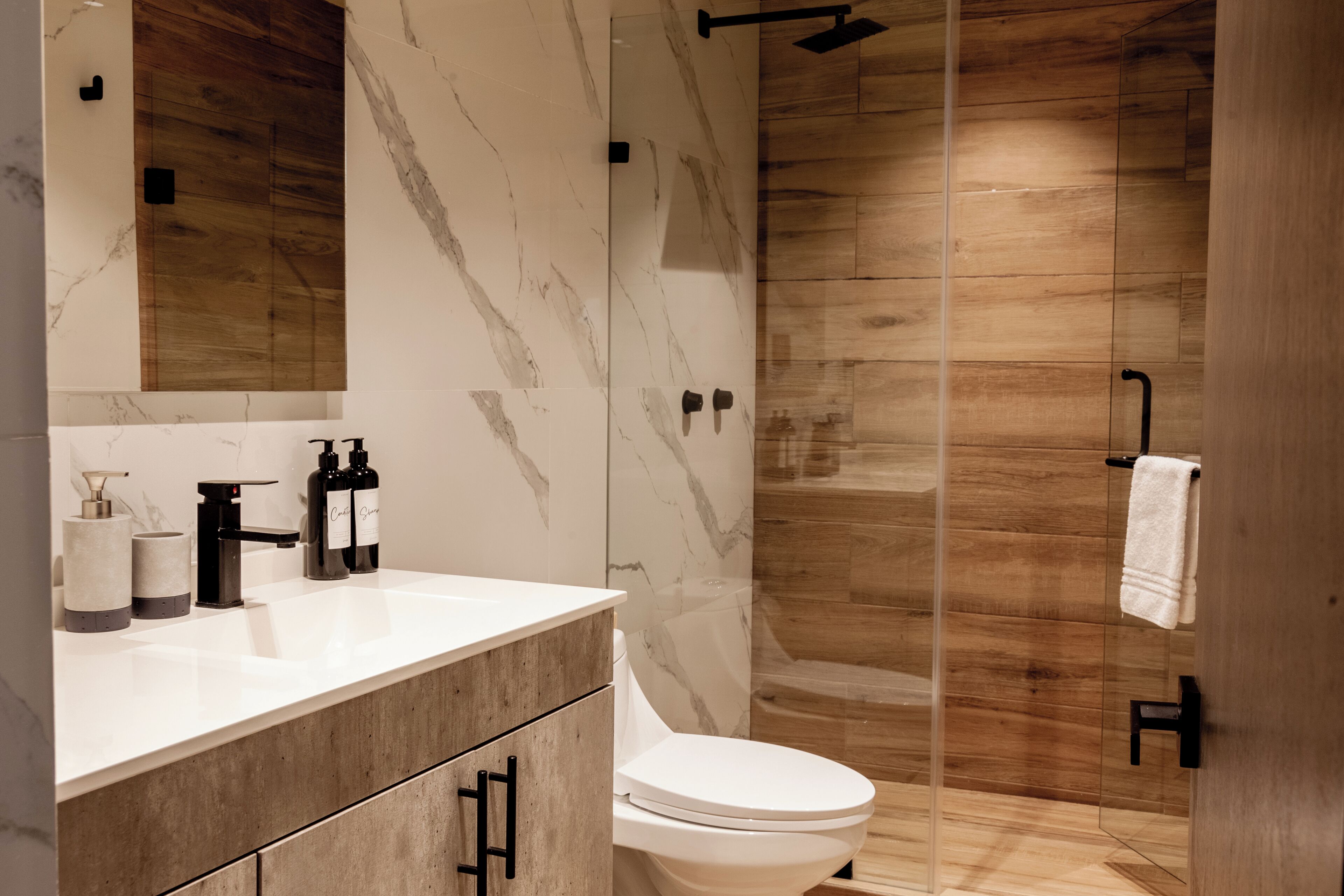 Ein modernes Badezimmer mit einem Holzbadezimmer-Möbel, einem weißen Waschbecken und einer gläsernen Duschkabine.