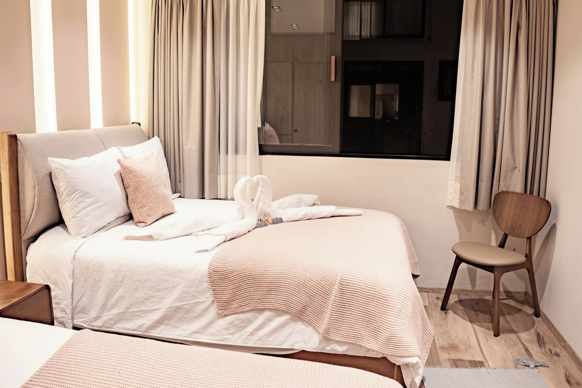 Una cama bien hecha con un edredón blanco y beige, un cabecero de madera y una silla con estructura de madera.