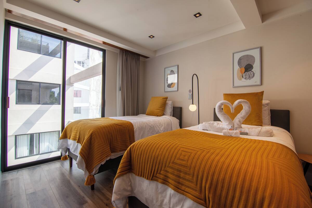 Habitación de hotel con dos camas, cada una con una manta marrón, un ventanal grande y vistas a edificios.