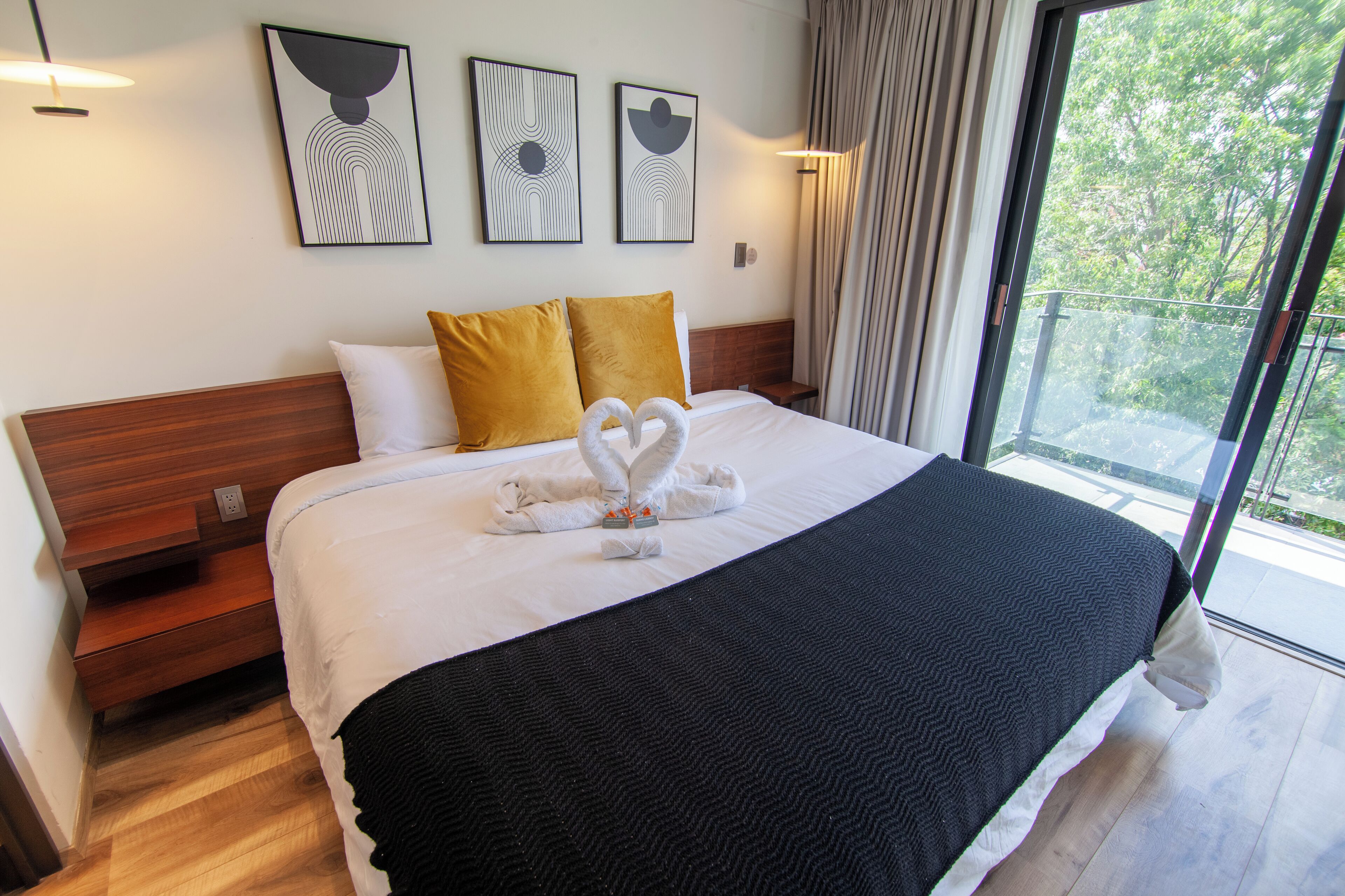 Une chambre d’hôtel avec un grand lit, deux oreillers, une couverture noire et deux serviettes disposées sur le lit en forme de cygne. Trois œuvres d’art encadrées sont accrochées au mur au-dessus du lit.