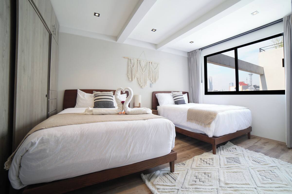 Una habitación de hotel moderna con dos camas, un ventanal grande y vistas a la ciudad.
