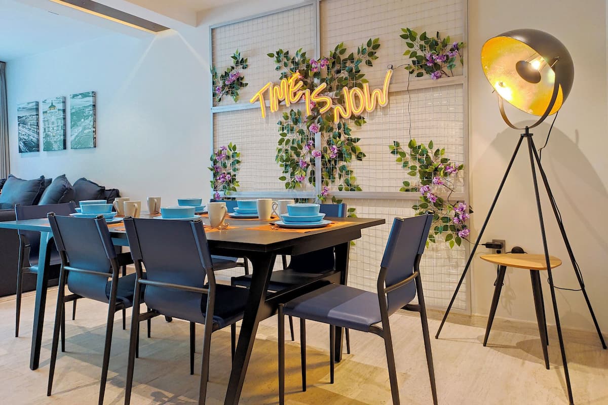 Un comedor moderno con un letrero de neón, una mesa puesta con platos azules y blancos, y una lámpara de pie.