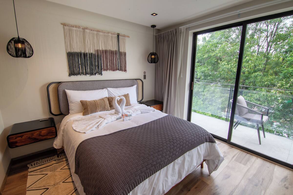 Un dormitorio con una cama grande, un balcón con una silla y vistas a zonas verdes.