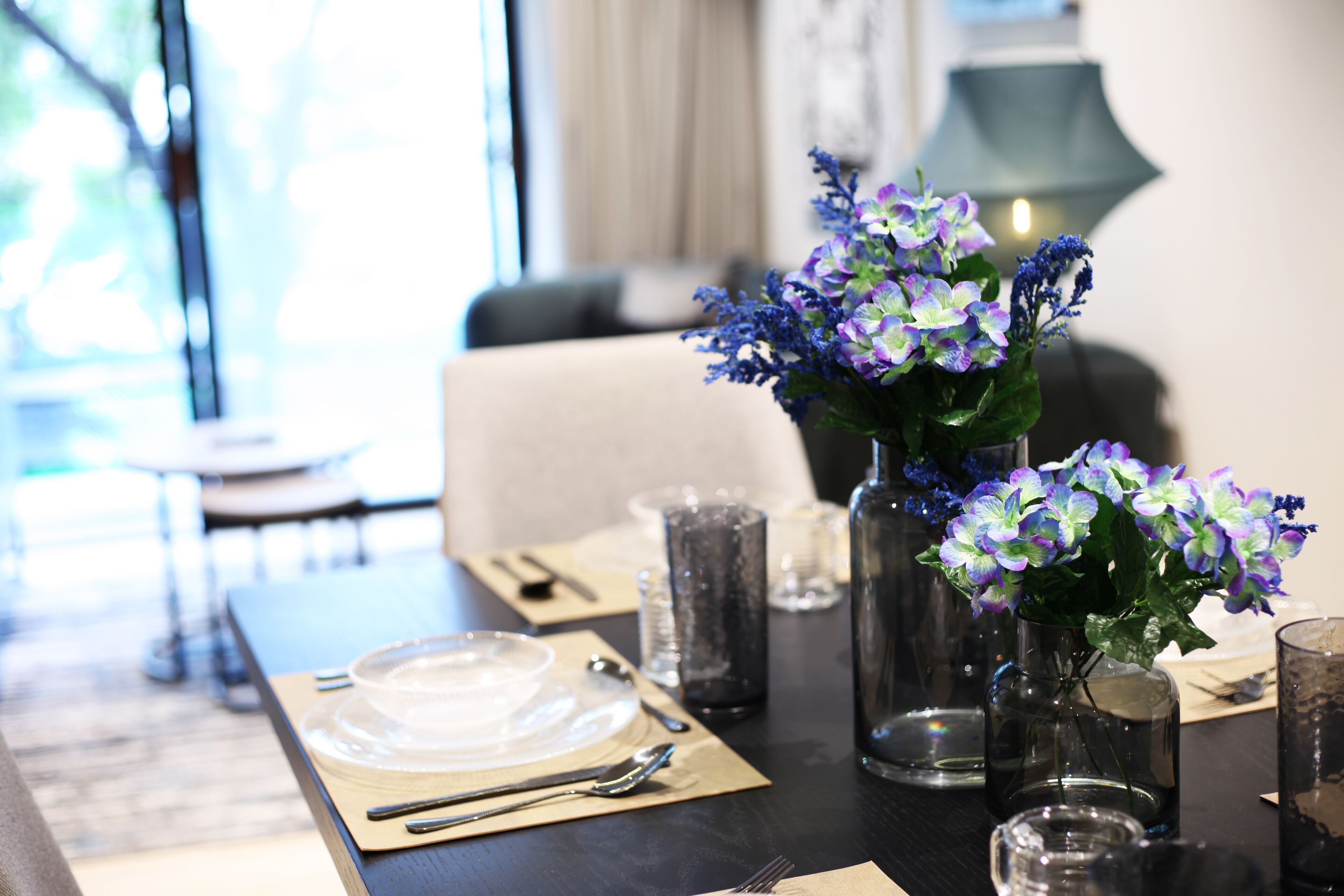 Una mesa de comedor dispuesta con platos, cubiertos y un jarrón con flores.