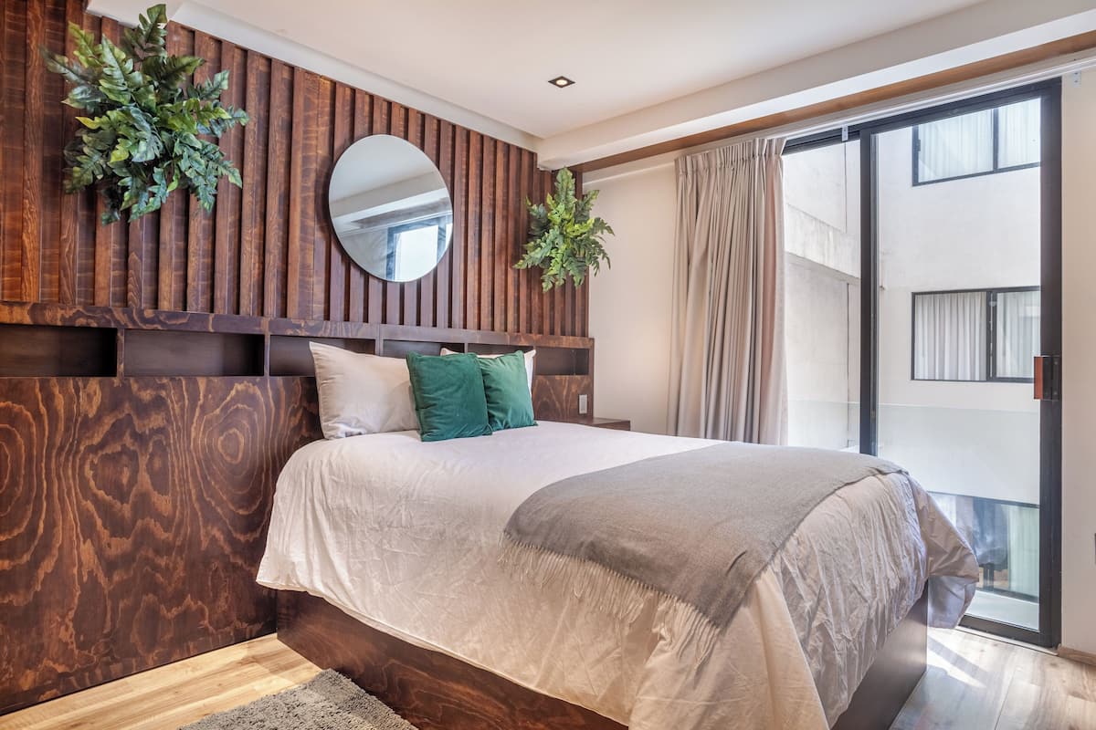 Un dormitorio con una cama grande, cabecera de madera, un espejo y vistas al exterior mediante una puerta corrediza de vidrio.